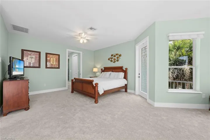 Carpeted bedroom featuring light green walls, a ceiling fan with light, a window with exterior foliage, and a glass-paneled door