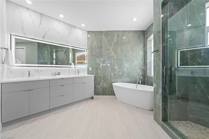 Spacious bathroom featuring a dual vanity with a lighted mirror, freestanding soaking tub, and a glass-enclosed shower