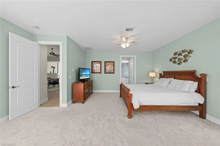 Spacious bedroom featuring light green walls, light-toned carpet flooring, a ceiling fan with integrated lighting, and white baseboards