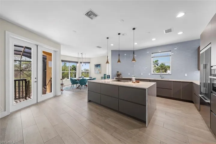 Modern kitchen featuring a large central island with a light-toned countertop, stainless steel appliances, a light blue subway tile backsplash, recessed lighting, and wood-finish flooring