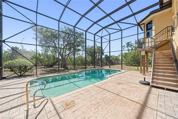 Screened enclosure featuring a freeform pool, stamped concrete patio, and a wooden exterior staircase