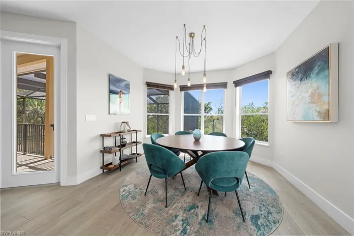 Dining area featuring light wood-finish flooring, a contemporary chandelier, multiple windows with natural light, and a single glass-paneled door