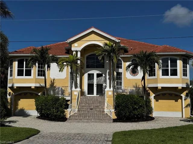 Mediterranean-inspired stucco exterior featuring a terra cotta tile roof, prominent bay windows, and a paver driveway