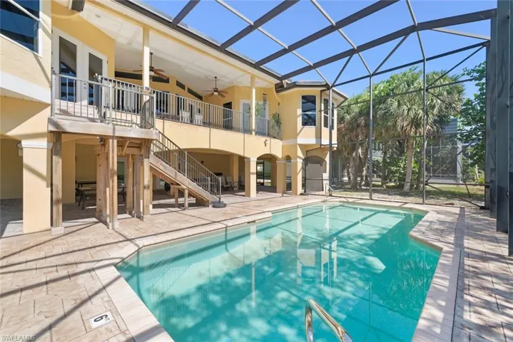 Screened-in outdoor pool featuring a paved deck, direct access to the elevated balcony, and a covered patio area