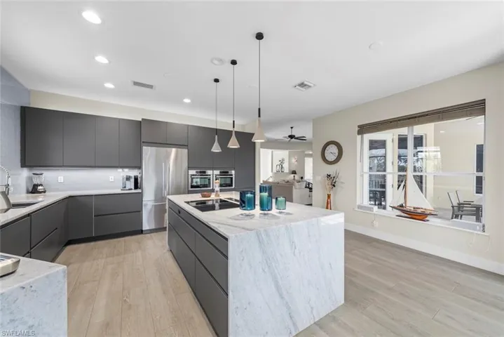 Modern kitchen featuring a waterfall island, integrated appliances, recessed lighting, wood-finish flooring, and a large window