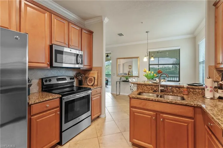 Kitchen featuring sink, light tile patterned floors, ornamental molding, stainless steel appliances, and light stone countertops