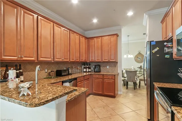 Kitchen featuring pendant lighting, appliances with stainless steel finishes, ornamental molding, kitchen peninsula, and dark stone counters