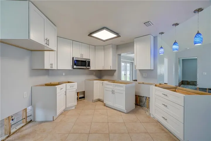 Kitchen with white cabinets, decorative light fixtures, and light tile patterned floors