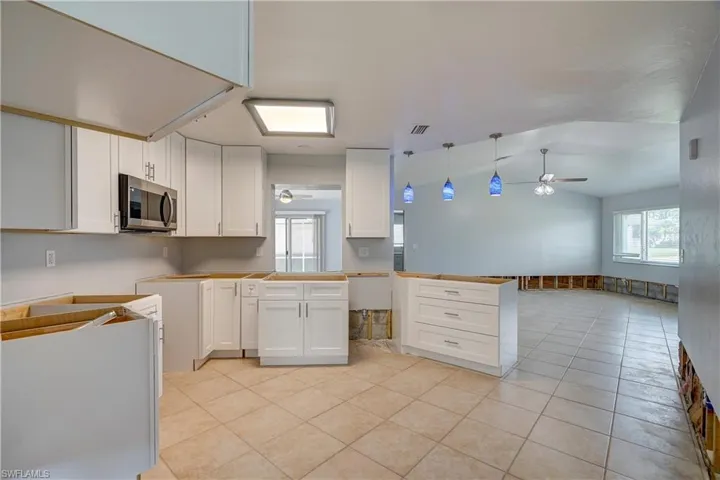 Kitchen with ceiling fan, white cabinets, hanging light fixtures, and vaulted ceiling