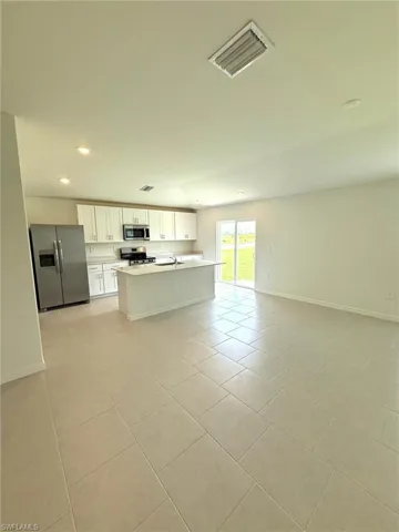 Kitchen with stainless steel appliances, open floor plan, light tile patterned floors, light countertops, and white cabinets