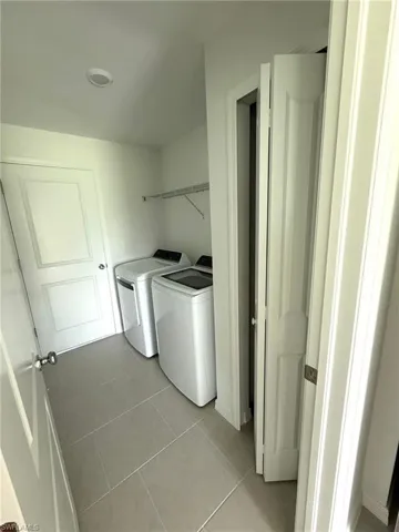 Laundry room with washer and clothes dryer and light tile patterned floors