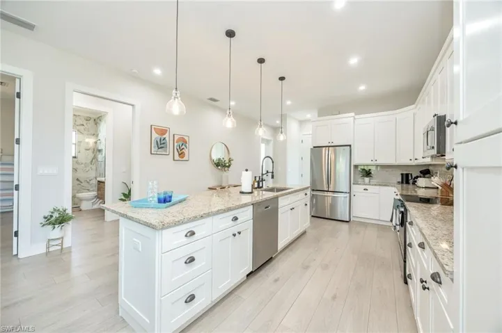 Spacious kitchen featuring white cabinetry, light-toned wood-finish flooring, and a large central island with a granite countertop and pendant lighting