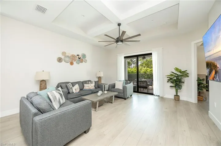 Spacious living area featuring light wood-finish flooring, a tray ceiling with a modern ceiling fan, and sliding glass doors opening to an outdoor patio