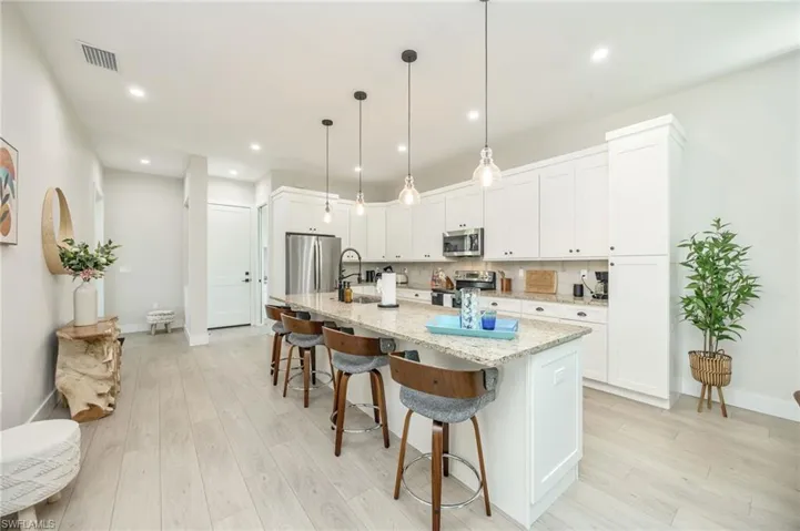 Modern kitchen featuring a large central island with seating, light granite countertops, white cabinetry with dark hardware, stainless steel appliances, and wood-finish flooring