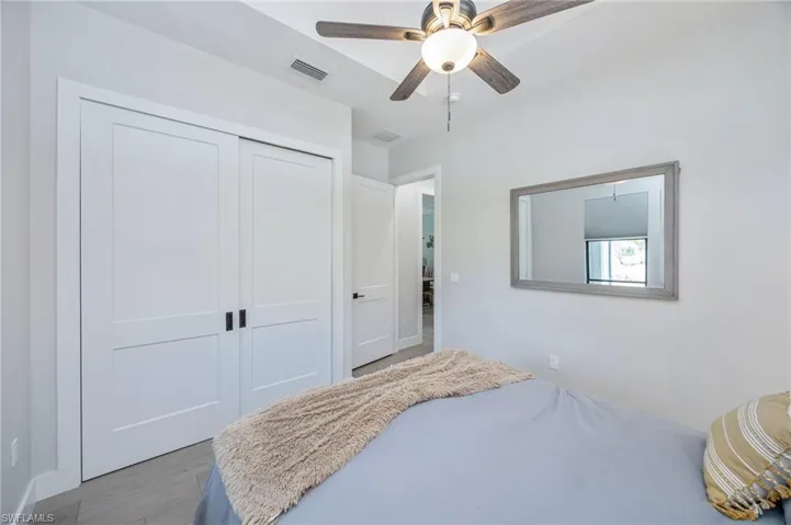 Bedroom featuring wood-finish flooring, a contemporary ceiling fan, and white sliding closet doors with black hardware