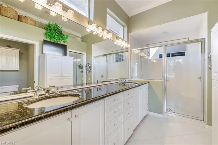 Full bath featuring double vanity, a shower stall, ornamental molding, and light tile patterned flooring