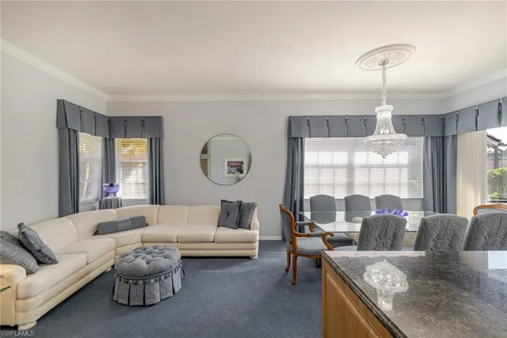 Living area featuring ornamental molding, dark colored carpet, plenty of natural light, and a chandelier