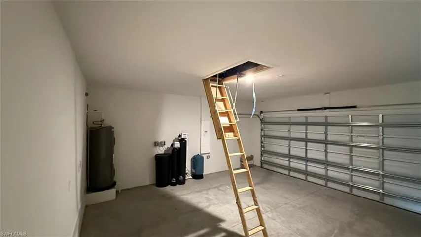 Spacious garage featuring a pull-down attic ladder, concrete flooring, and a large metal garage door