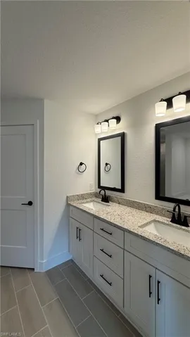 Dual vanity featuring white shaker cabinetry with black hardware, granite countertops, and undermount sinks