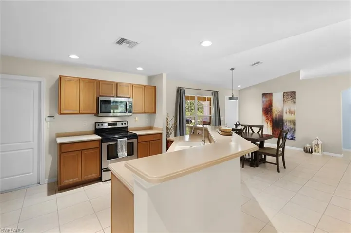Kitchen with vaulted ceiling, light tile flooring, stainless steel appliances, hanging light fixtures, and an island with sink
