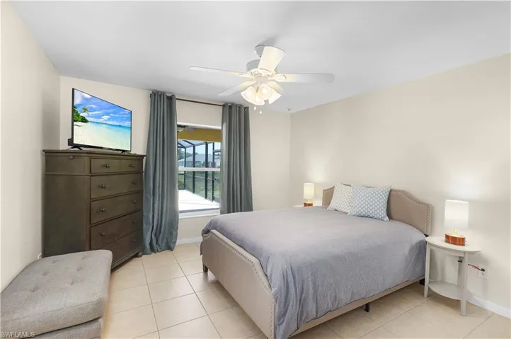 Tiled primary bedroom with ceiling fan overlooking pool
