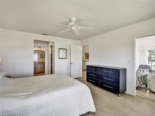 Bedroom with ceiling fan, light tile patterned floors, and ensuite bath