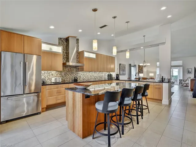 Kitchen featuring freestanding refrigerator, pendant lighting, light tile patterned floors, a breakfast bar, and backsplash