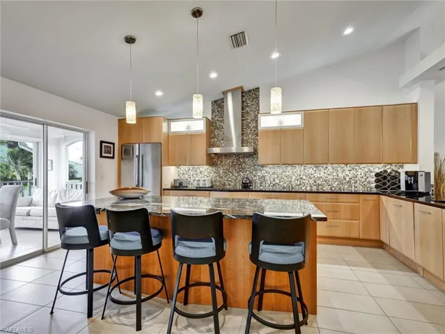 Kitchen with lofted ceiling, decorative backsplash, light tile patterned floors, dark stone countertops, and recessed lighting