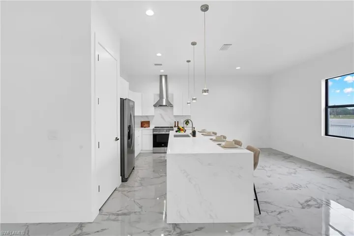 Sleek kitchen featuring a large waterfall island with integrated seating, white cabinetry, stainless steel appliances, and polished tile flooring