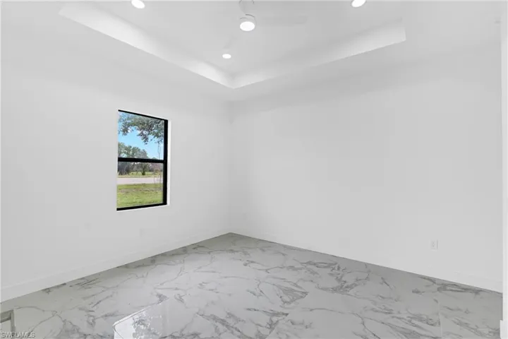 Spacious room featuring large format marble-look tile flooring, a tray ceiling with recessed lighting, and a modern ceiling fan