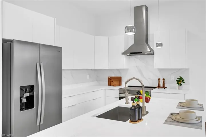 Modern kitchen featuring stainless steel appliances, white cabinetry, a large kitchen island with an integrated sink, a sleek range hood, and pendant lighting