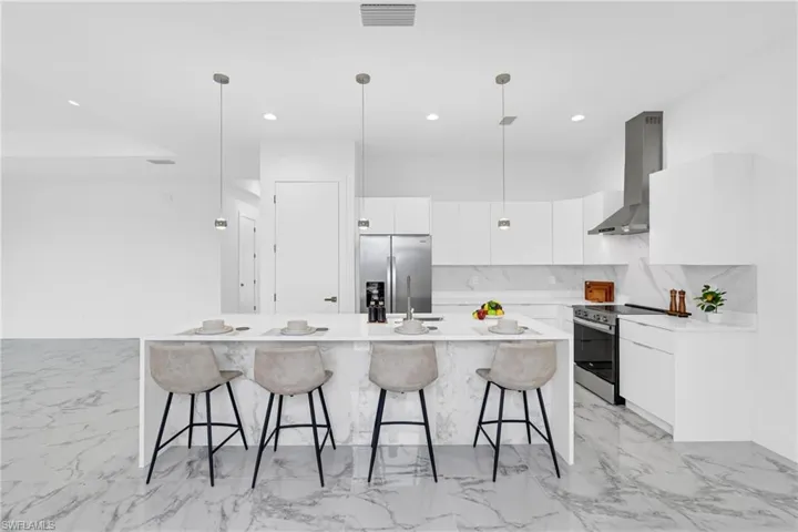 Gourmet kitchen featuring a waterfall island, stainless steel appliances, pendant lighting, built-in cabinetry, and large format marble-look flooring