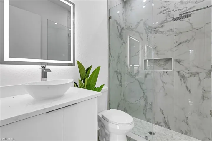 Modern bathroom featuring a glass-enclosed shower with marble-look tile, a built-in shower niche, and a rain shower head