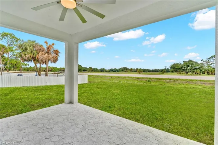 Covered patio featuring a ceiling fan with light fixture, textured concrete flooring, and white support columns