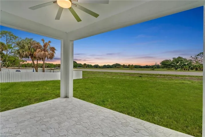 Covered patio featuring a ceiling fan with light fixture, textured concrete flooring, and an expansive grassy area