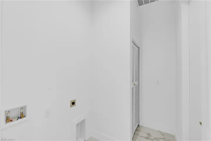 Dedicated laundry area featuring white walls, a louvered bifold door, and marble-patterned flooring