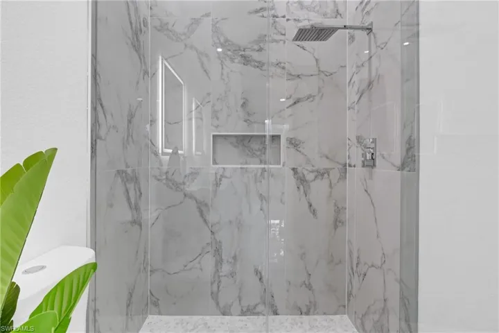 Modern shower enclosure featuring large-format marbled tile, a rainfall shower head, chrome fixtures, an integrated niche, and a clear glass partition