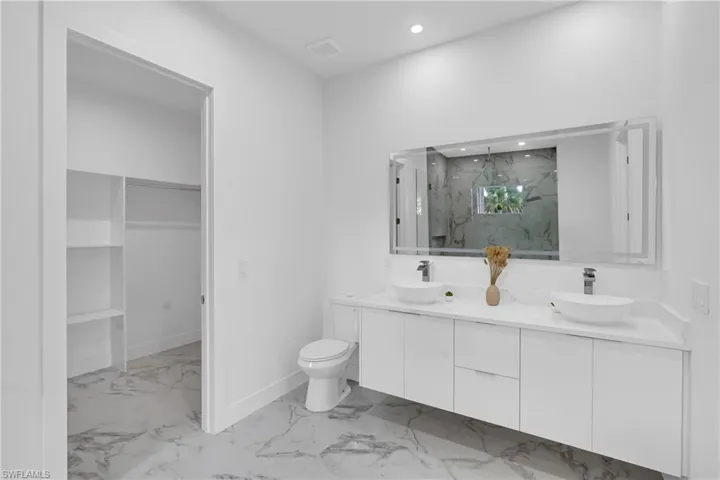 Bathroom featuring a dual vanity with white vessel sinks, a large wall-mounted mirror, and marble-look floor tiles