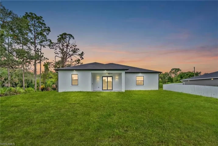 Expansive rear yard featuring a manicured lawn, a modern stucco exterior, and a covered patio with sliding glass doors