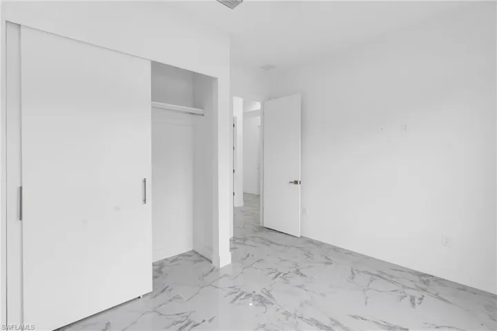Spacious room with white walls, sliding closet doors with brushed metal pulls, and white-veined stone-finish flooring