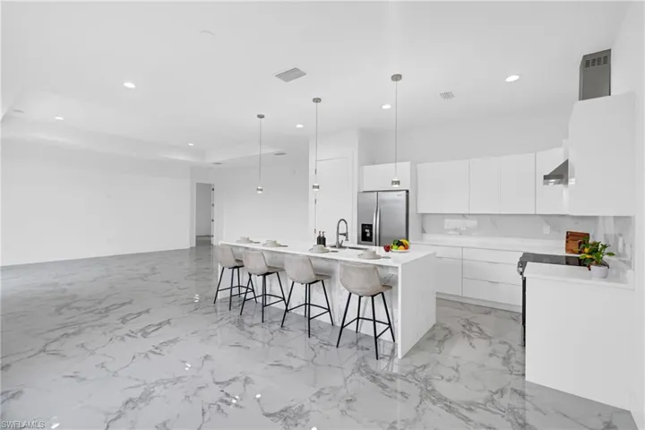 Open-concept kitchen featuring an oversized island with seating, pendant lighting, stainless steel appliances, and white cabinetry