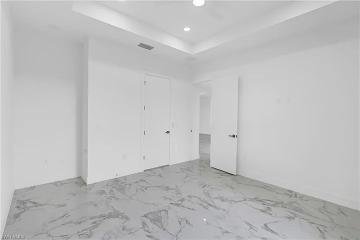 Spacious room featuring large format marble-look tile flooring, white walls, and a tray ceiling with recessed lighting