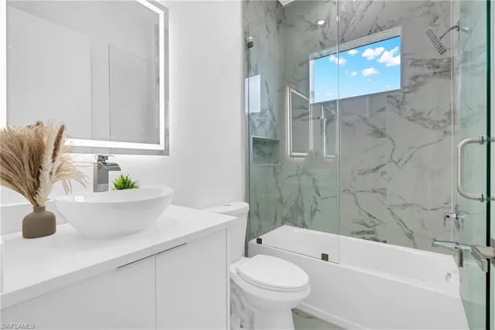 Contemporary bathroom featuring a floating vanity with a vessel sink, an illuminated mirror, a toilet, a soaking tub, and a glass-enclosed shower with large format marble-look tiling