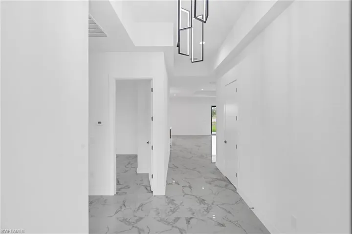 Entryway featuring large format grey and white marble-look tile flooring, contemporary geometric chandelier, recessed lighting, and white interior doors with satin nickel hardware