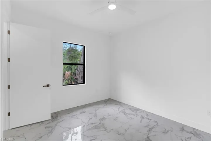 Spacious room featuring large format tile flooring, a contemporary ceiling fan with integrated lighting, a substantial window with dark trim, clean white walls, and a solid interior door with dark hardware