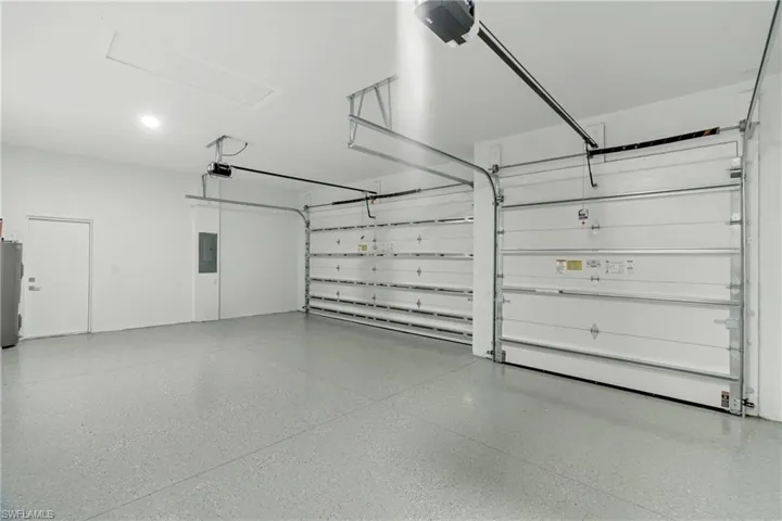 Three-car garage featuring a speckled epoxy floor coating, two overhead garage doors, an access panel, and a side access door