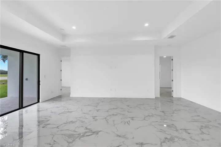 Spacious interior with large format marble-look tile flooring, white walls, and a tray ceiling with recessed lighting