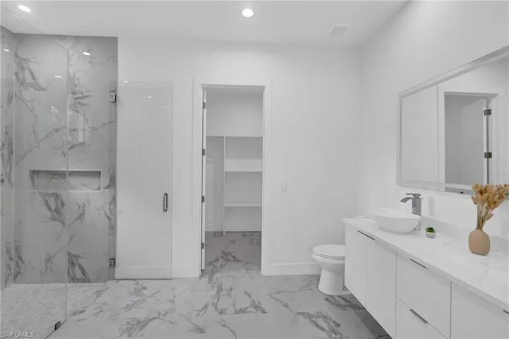Spacious bathroom featuring a glass-enclosed shower with marble-style tile surround and built-in niche, a double vanity with a vessel sink and quartz countertop, a large framed mirror, and marble-style tile flooring