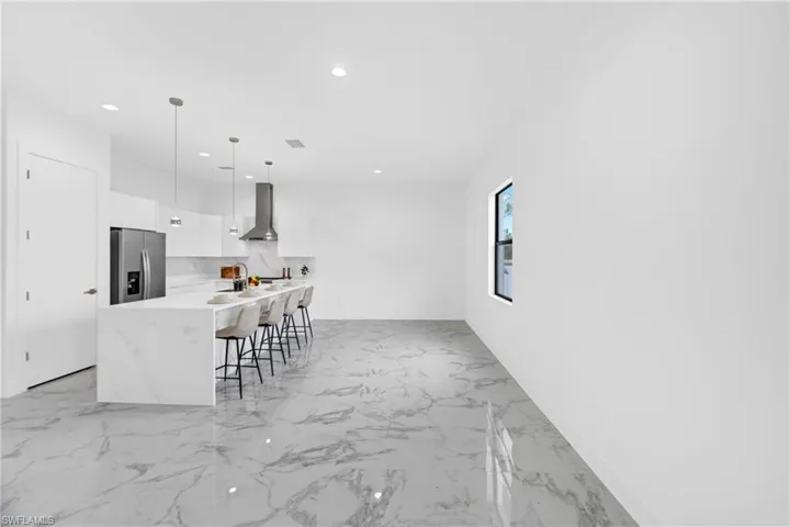 Modern open-concept kitchen featuring an oversized island with waterfall countertops, stainless steel appliances, and sleek white cabinetry