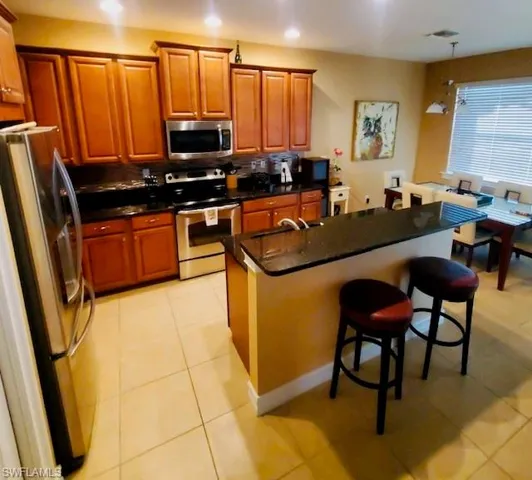 Kitchen featuring pendant lighting, stainless steel appliances, light tile patterned flooring, a kitchen breakfast bar, and a kitchen island with sink